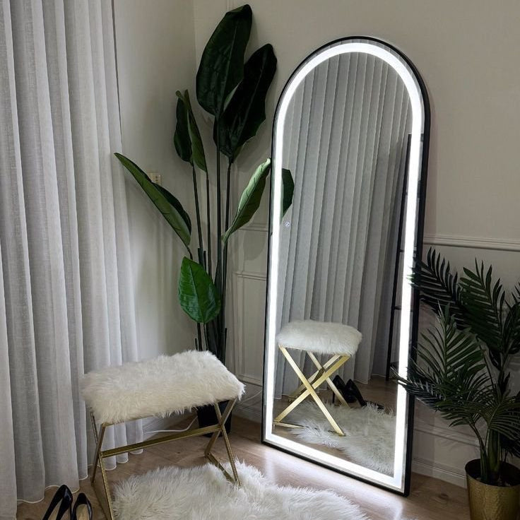 Full-length mirror with LED lighting on a white rug in a room with plants and a bench.