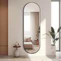 Full-length mirror leaning against a wall in a modern interior setting with a plant and small table.