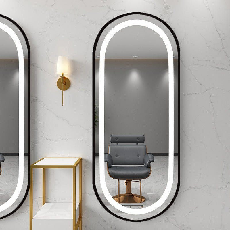 Oval-shaped mirror with illuminated frame on a wall with a chair reflection.