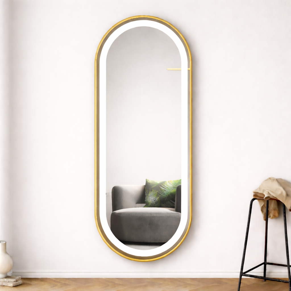 Oval-shaped mirror with gold frame on a white wall in a room with a gray sofa and a black stool.