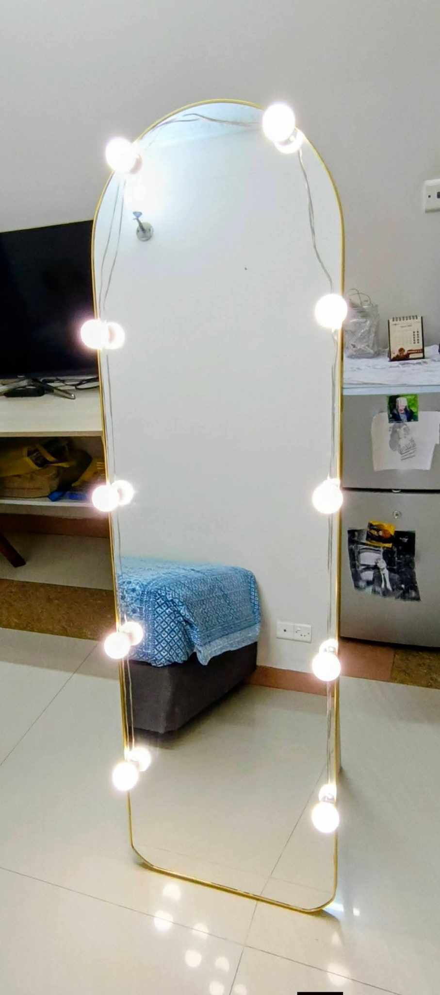 Full-length mirror with decorative lights on a tiled floor.