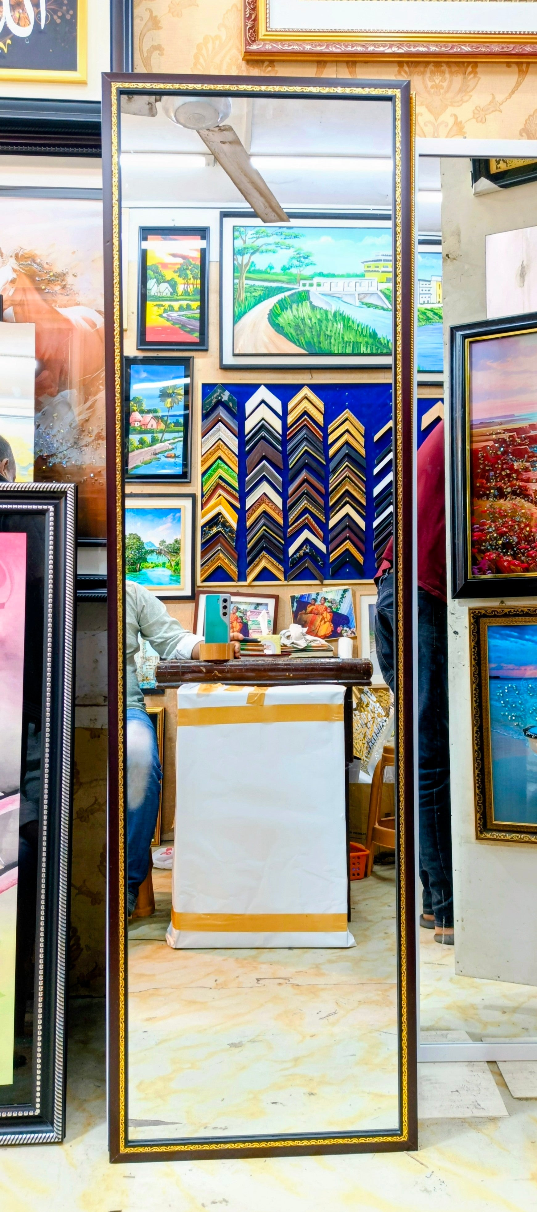 Framed artwork on display in a store with a mirror reflecting the interior.